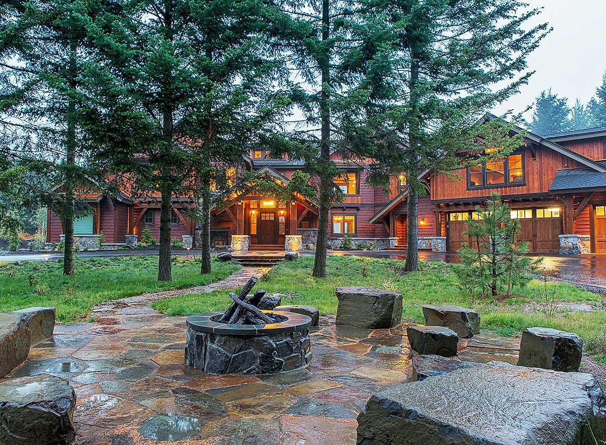 Modern mountain lodge style house exterior with stone-clad foundation, wood siding, covered entry, and multiple garage bays.