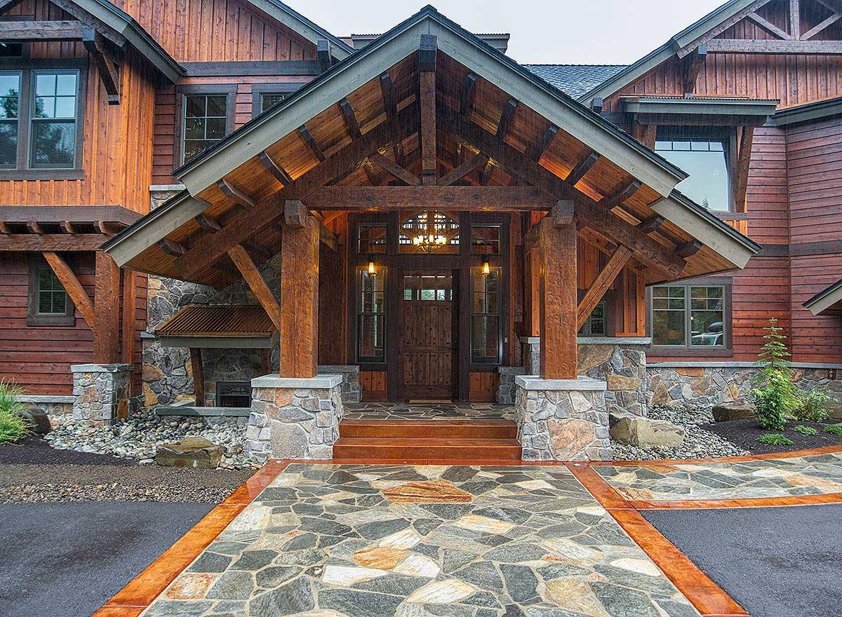 House plan exterior: Timber-frame entrance with stone base, gabled roof, wood siding, and large windows.