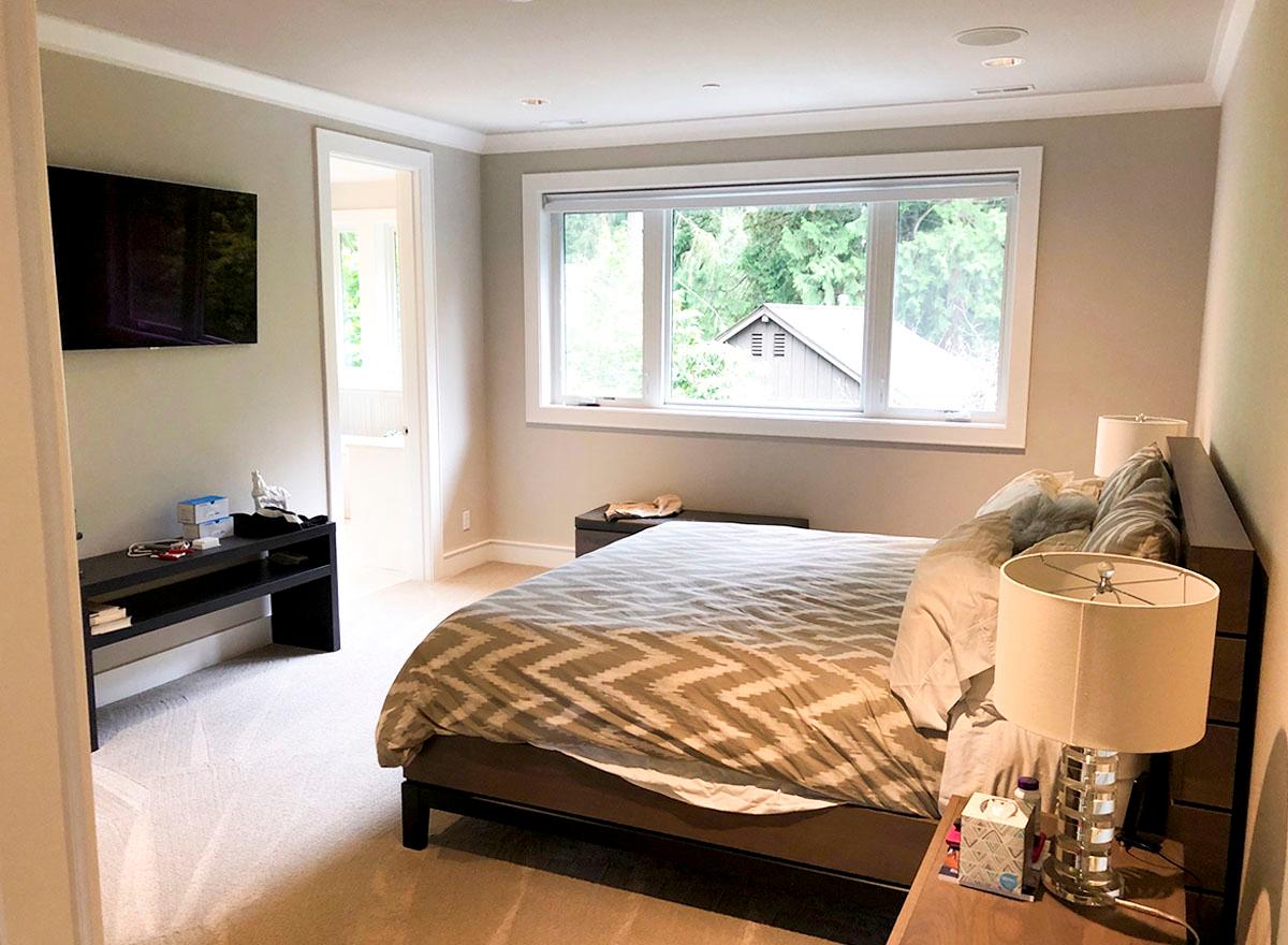 Bedroom with king size bed, large window, and wall-mounted television. Ensuite bathroom visible through doorway.