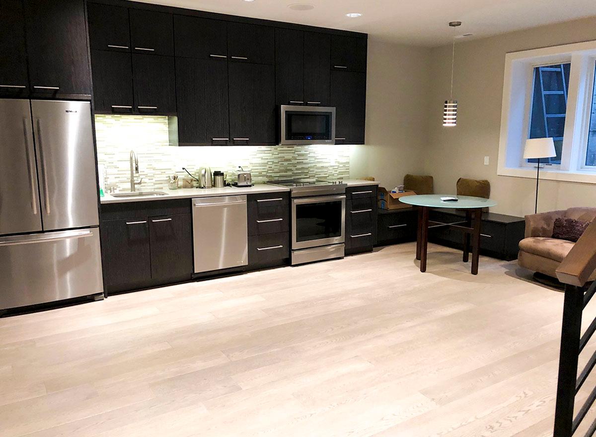 Kitchen with dark wood cabinetry, stainless steel appliances, glass tile backsplash, small dining table, and seating area.