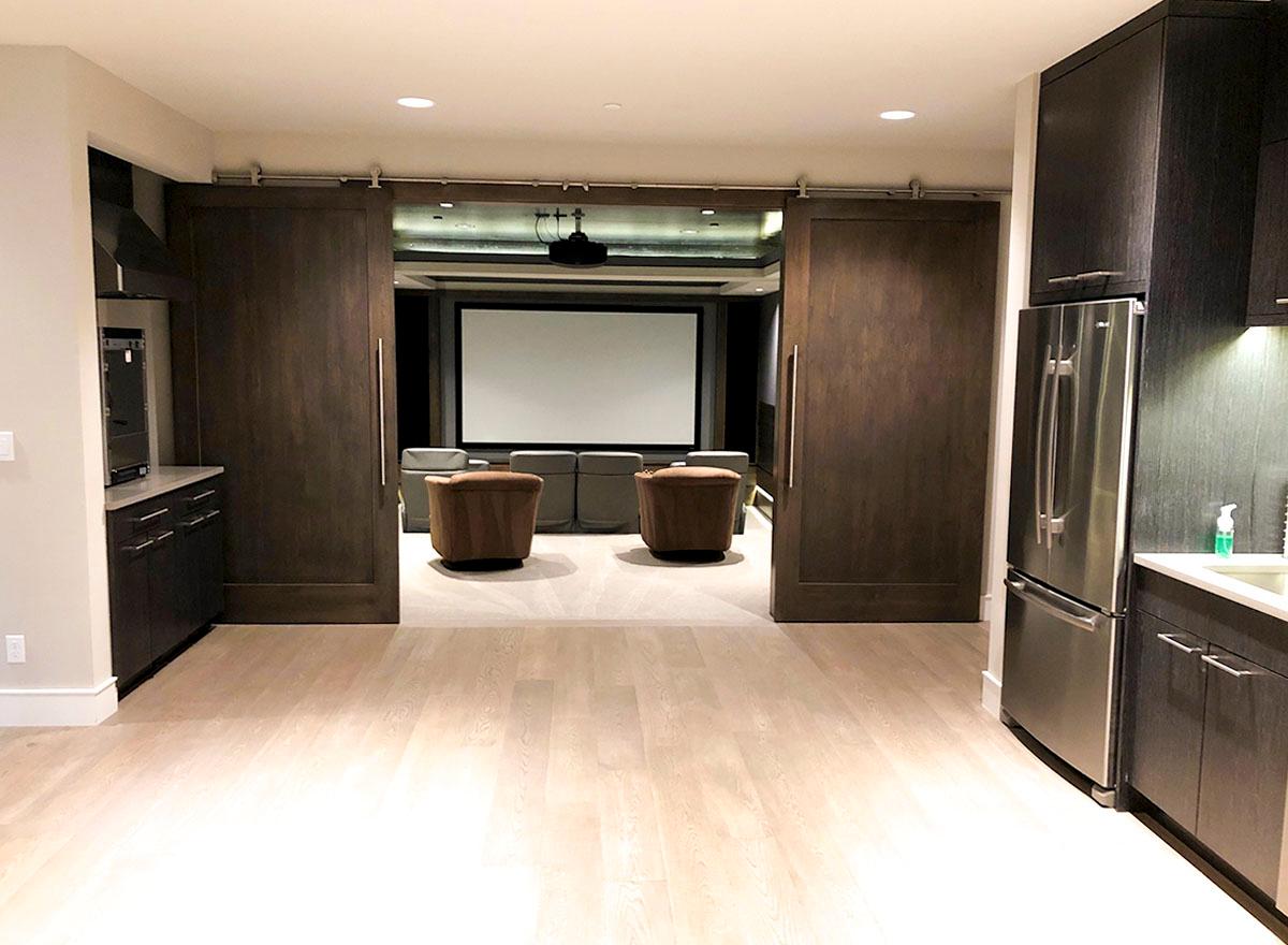 Home theater with large screen, tiered seating, and dark wood sliding barn doors.