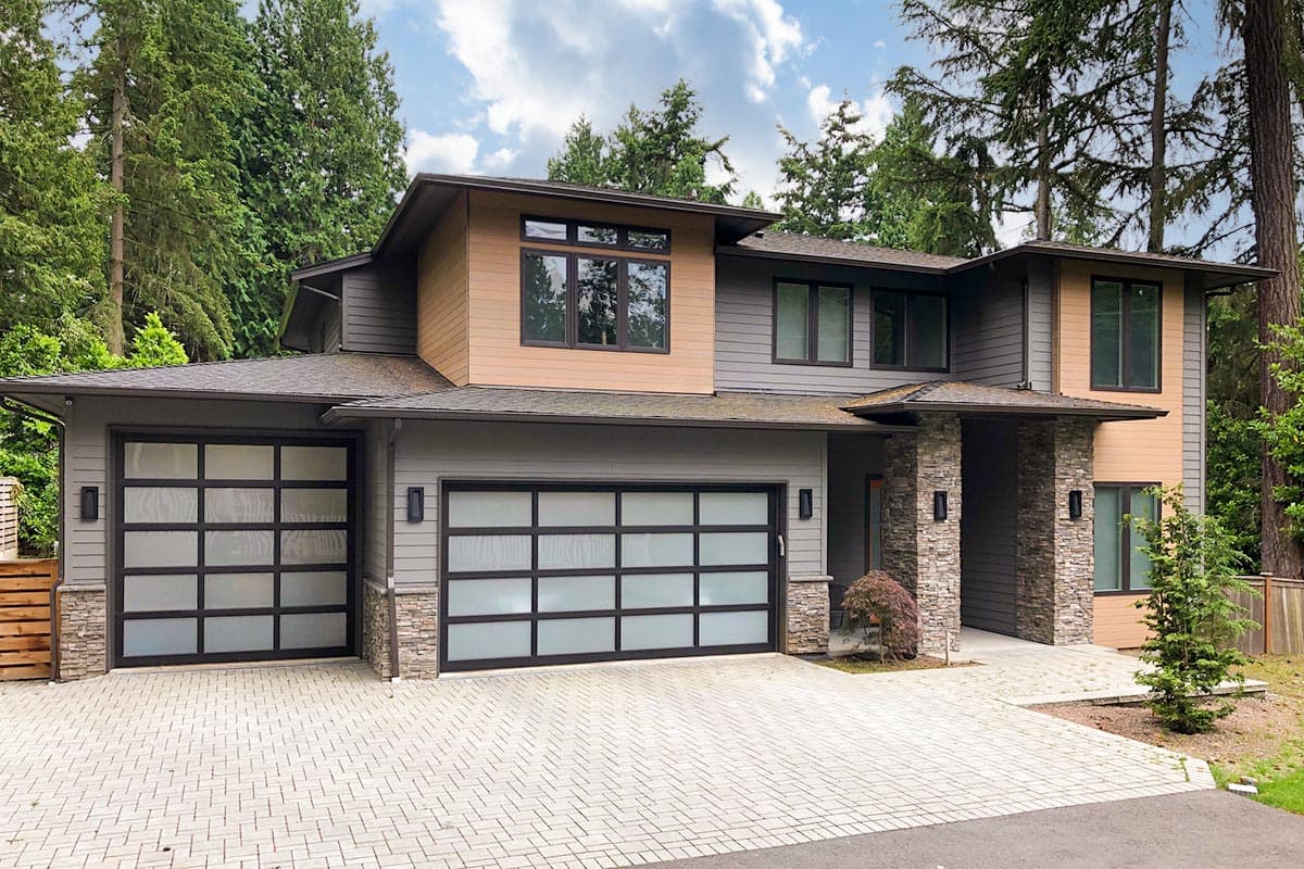 House plan exterior. Two-story modern style home with flat roof, attached garage, and stone accent pillars. Features large windows and siding.