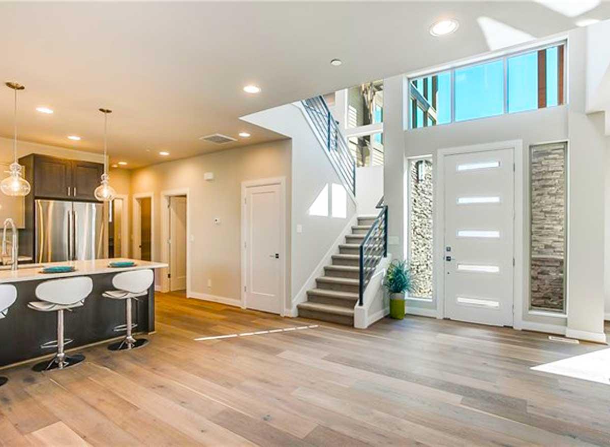 Interior view of an open-concept home with a kitchen island, modern staircase, and large entryway windows.