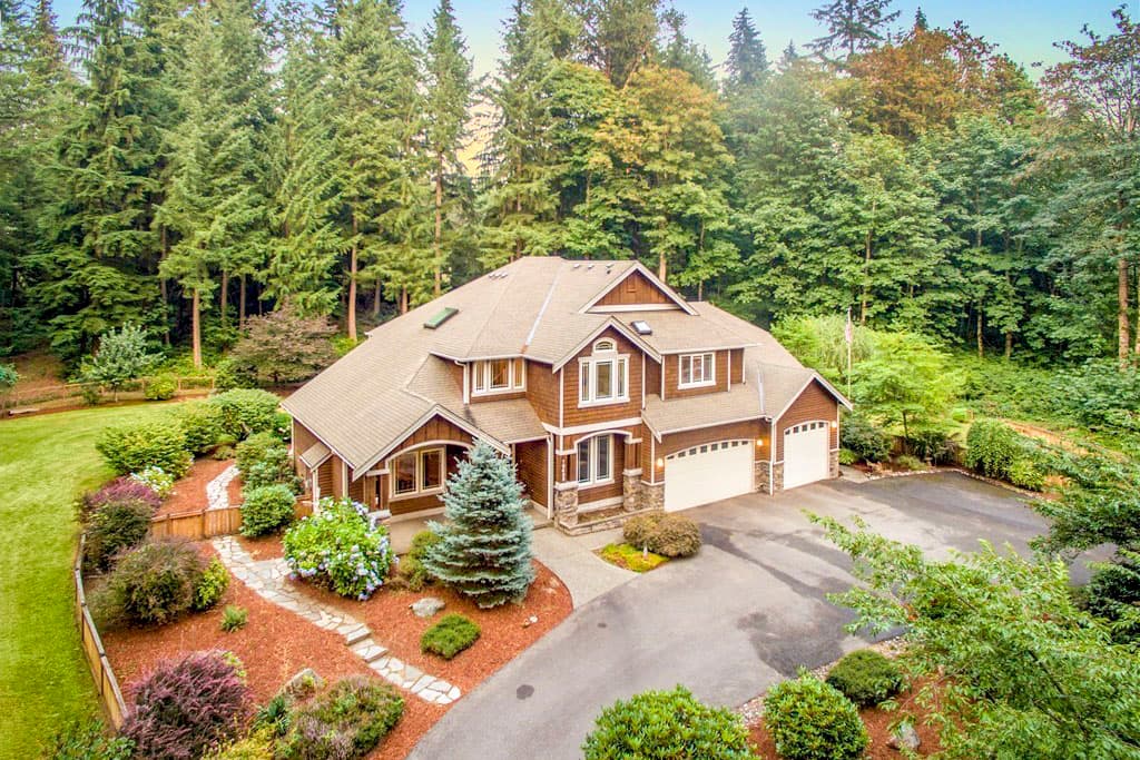 House plan exterior: two-story, brown wood siding, hip roof, three-car garage, covered entry, dormers.