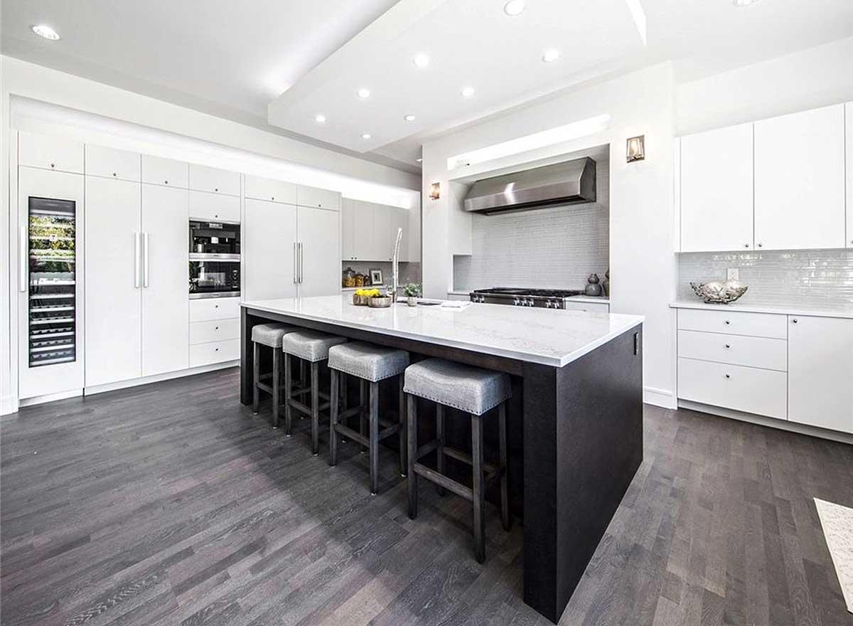 Kitchen with large island, seating for four, wine fridge, modern cabinetry, stainless steel range hood and backsplash.