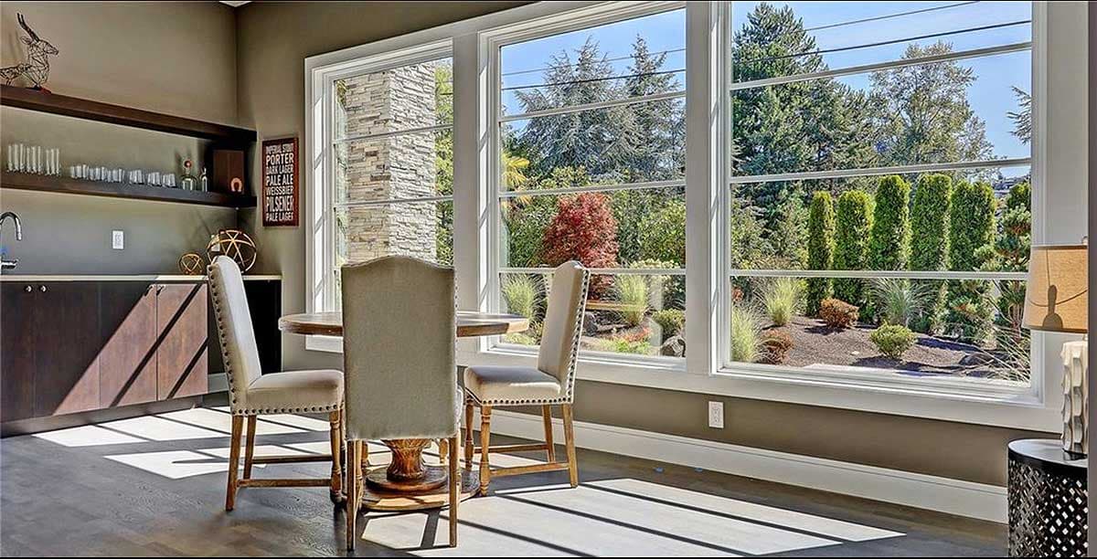 Interior view of a dining nook with built-in cabinetry, a round table, chairs, and large casement windows overlooking a garden.