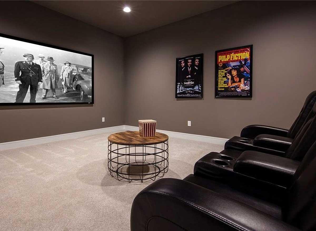 Home theater room with large screen, leather recliners, movie posters, and round coffee table.