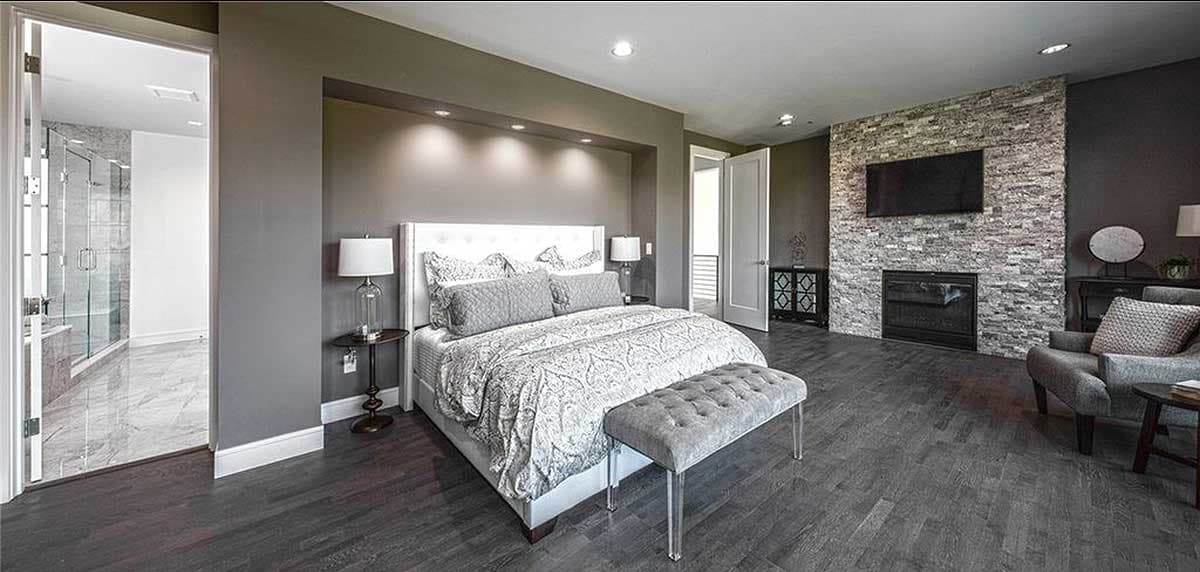 Bedroom with king bed, stone fireplace, attached glass-door shower, and dark wood flooring.