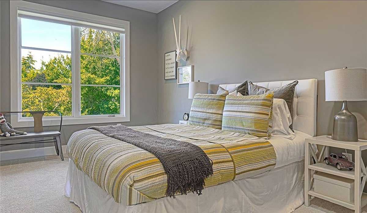Bedroom with large window overlooking trees, striped bedding, and a tufted headboard.