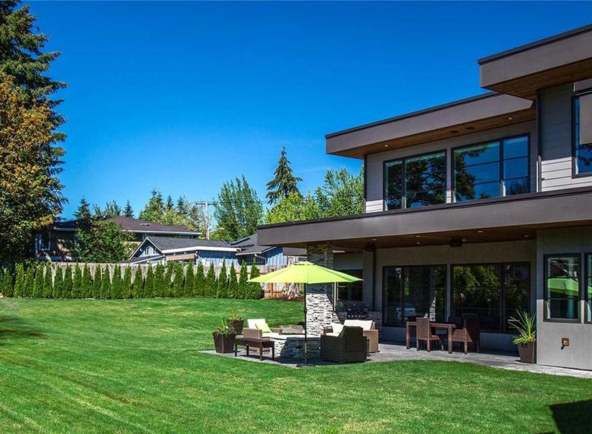 Modern house plan exterior with cantilevered upper story, large windows, and covered patio with stone fireplace.