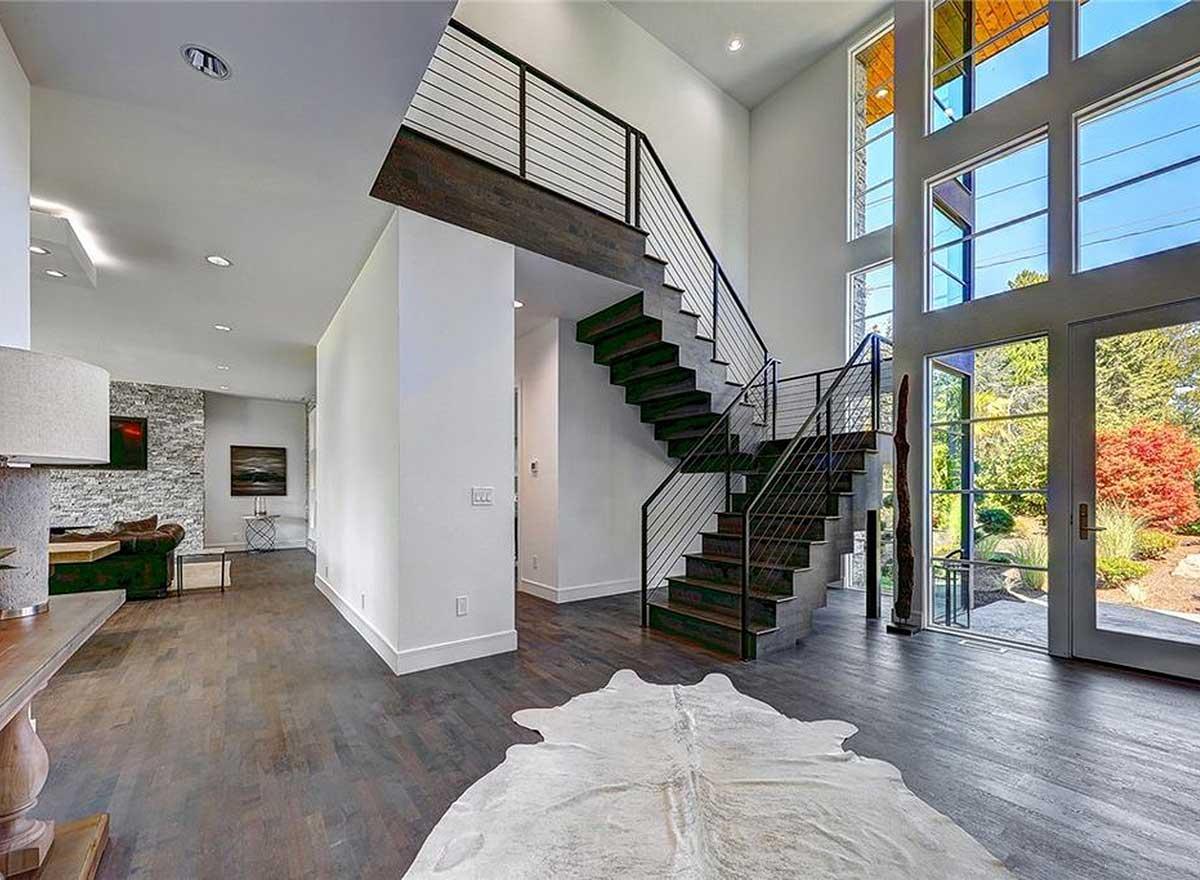 Interior view of a modern home with a floating staircase, minimalist railings, and a wall of large windows.