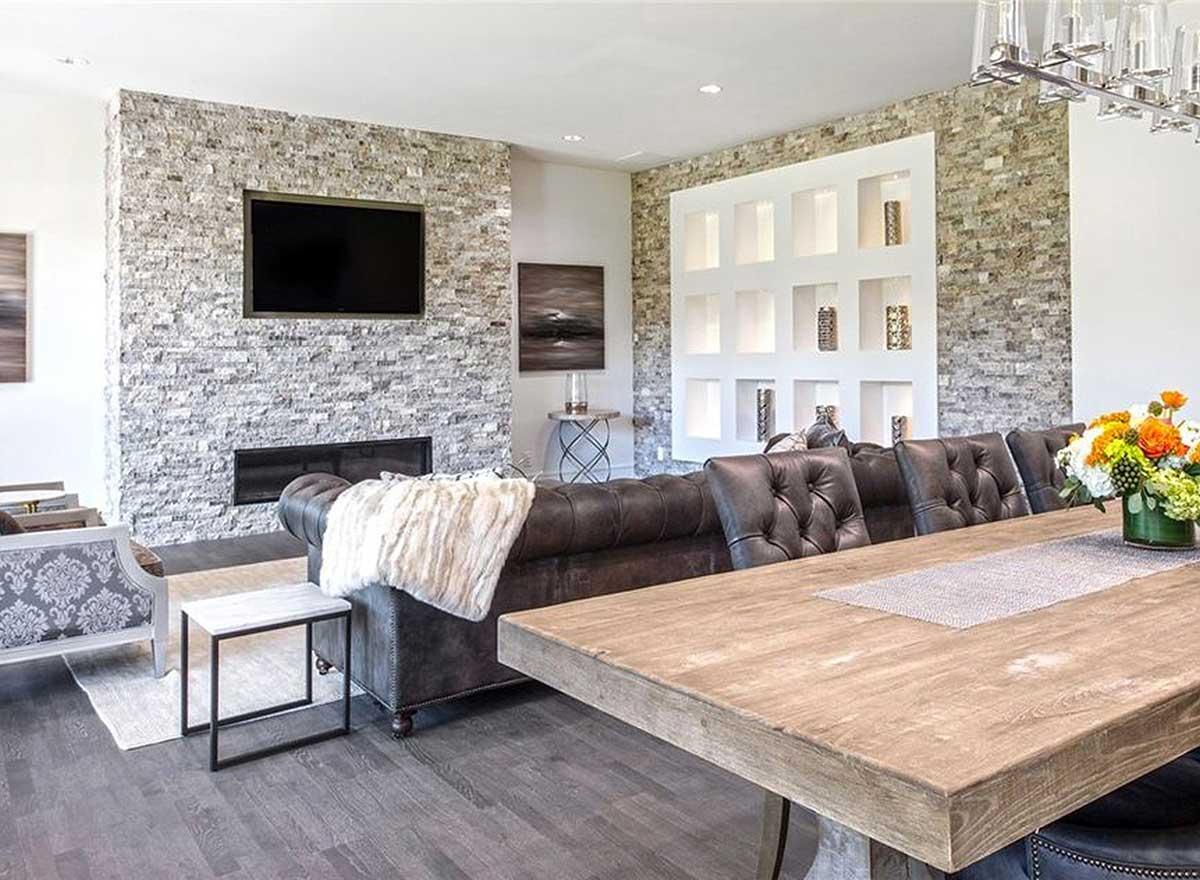 Living and dining area with stone fireplace, TV, tufted sofa, and wooden dining table.