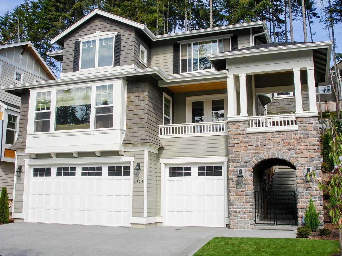 Exterior view of a two-story house plan with dual garages, stone archway, bay window, and covered porch with columns.