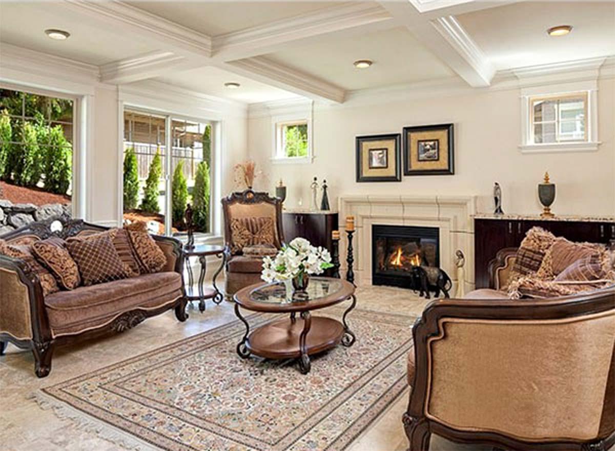 Living room interior with coffered ceiling, fireplace, large windows with garden views, ornate furniture, and patterned rug.