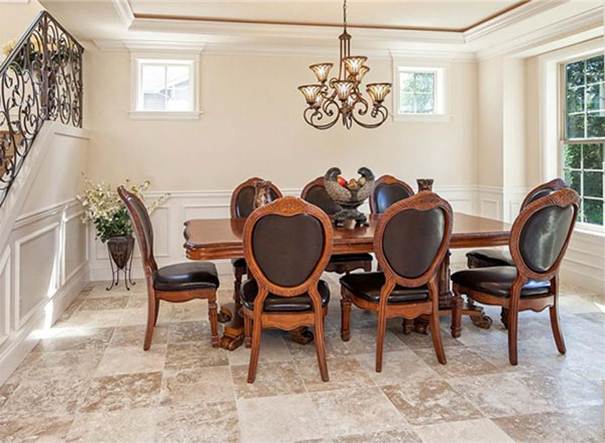 Dining room with wood table, ornate chairs, decorative chandelier, wainscoting, and tiled floor.