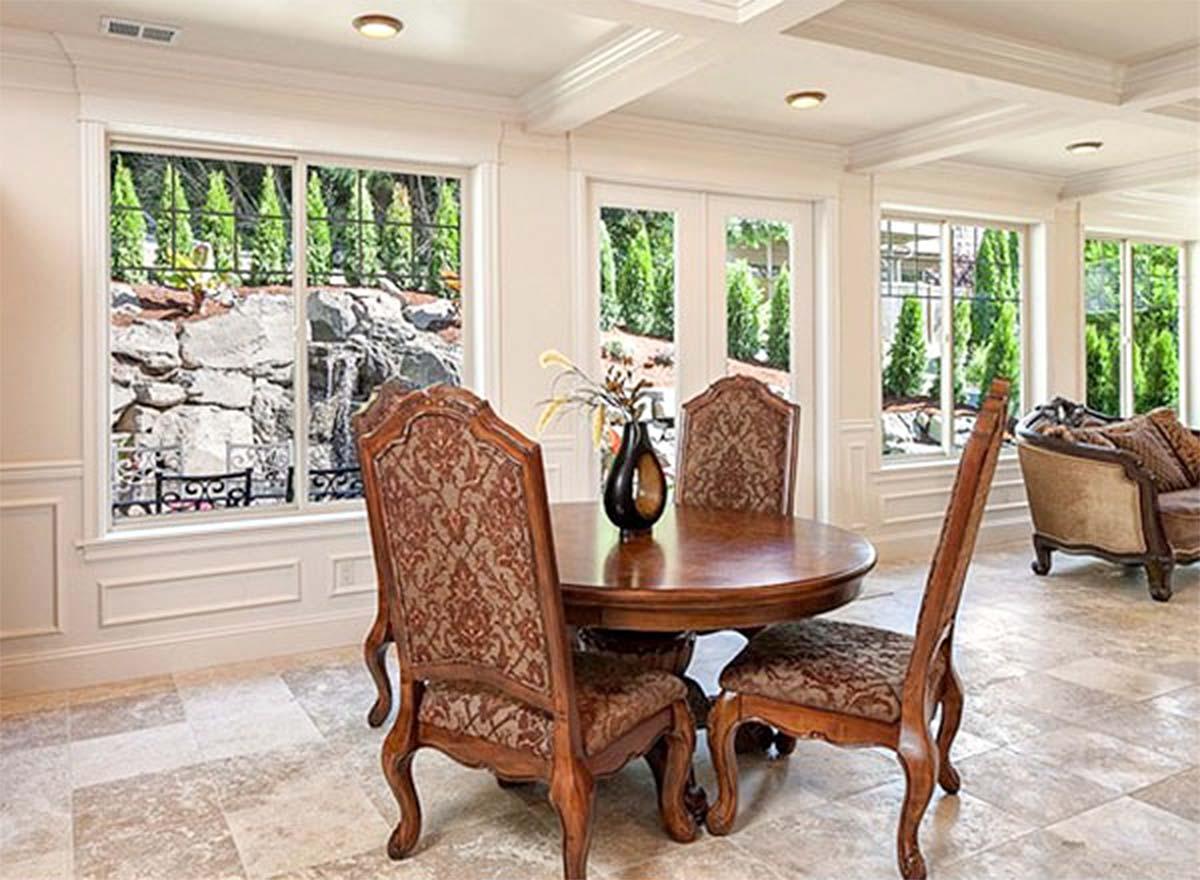 Dining area with round wood table, upholstered chairs, and windows overlooking a rock garden with a waterfall.