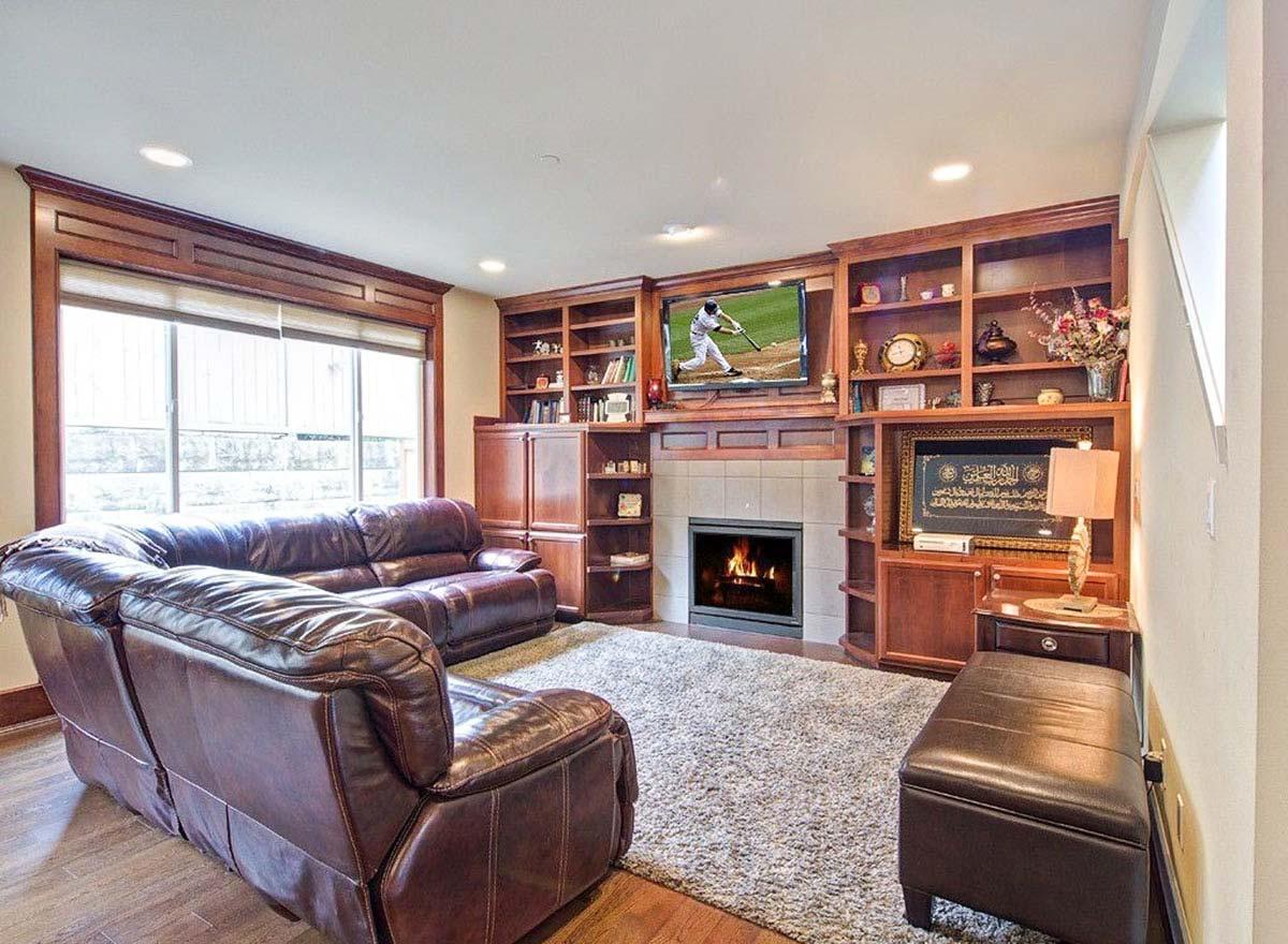 Living room with built-in wood bookcases, fireplace, TV, leather sofa, and large window.