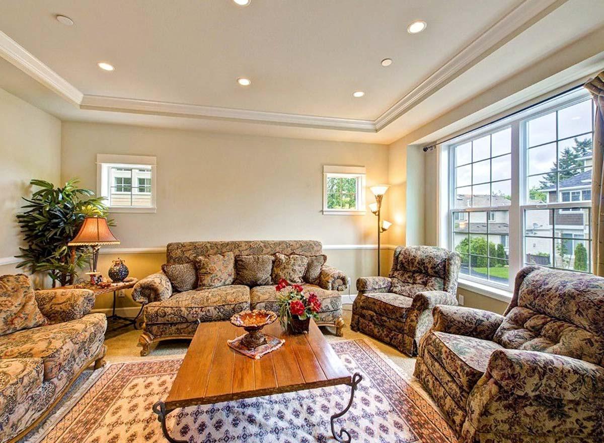 Living room interior with coffered ceiling, large windows, patterned sofa and armchairs, and coffee table.