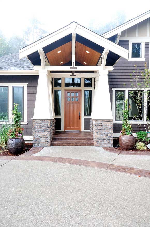 Craftsman-style house exterior with a covered porch, stone pillar bases, wood-paneled ceiling, and multi-pane glass door.