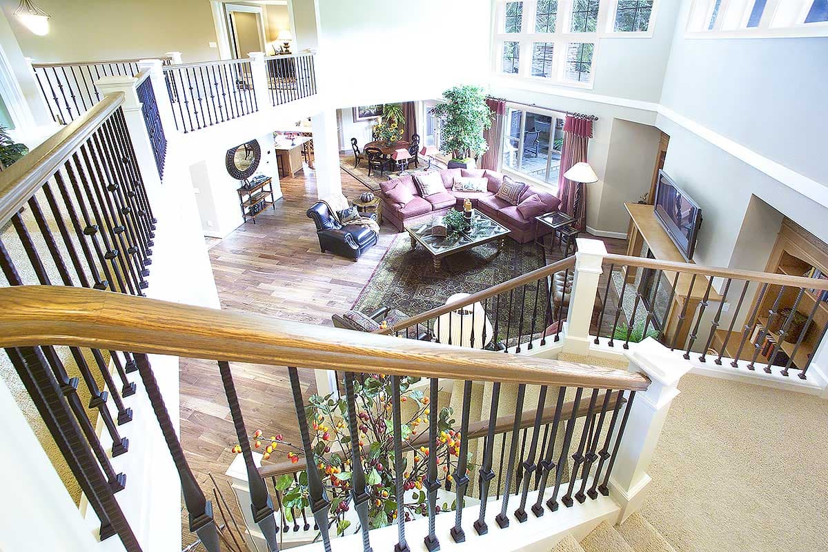View from landing of living room with vaulted ceiling, large windows, fireplace, and open staircase with wrought iron railing.