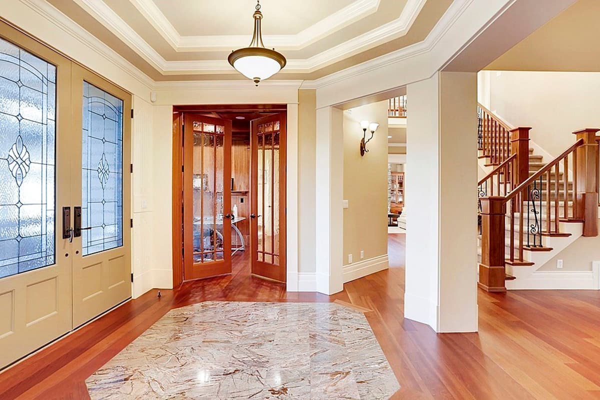 Entryway with double doors featuring frosted glass, hardwood floors, marble inlay, and a wood staircase with wrought iron balusters.