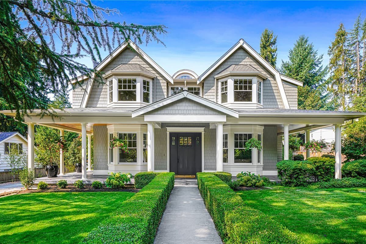 House plan exterior. Two-story Craftsman home with a gabled roof, dormers, and a wraparound porch with columns and bay windows.