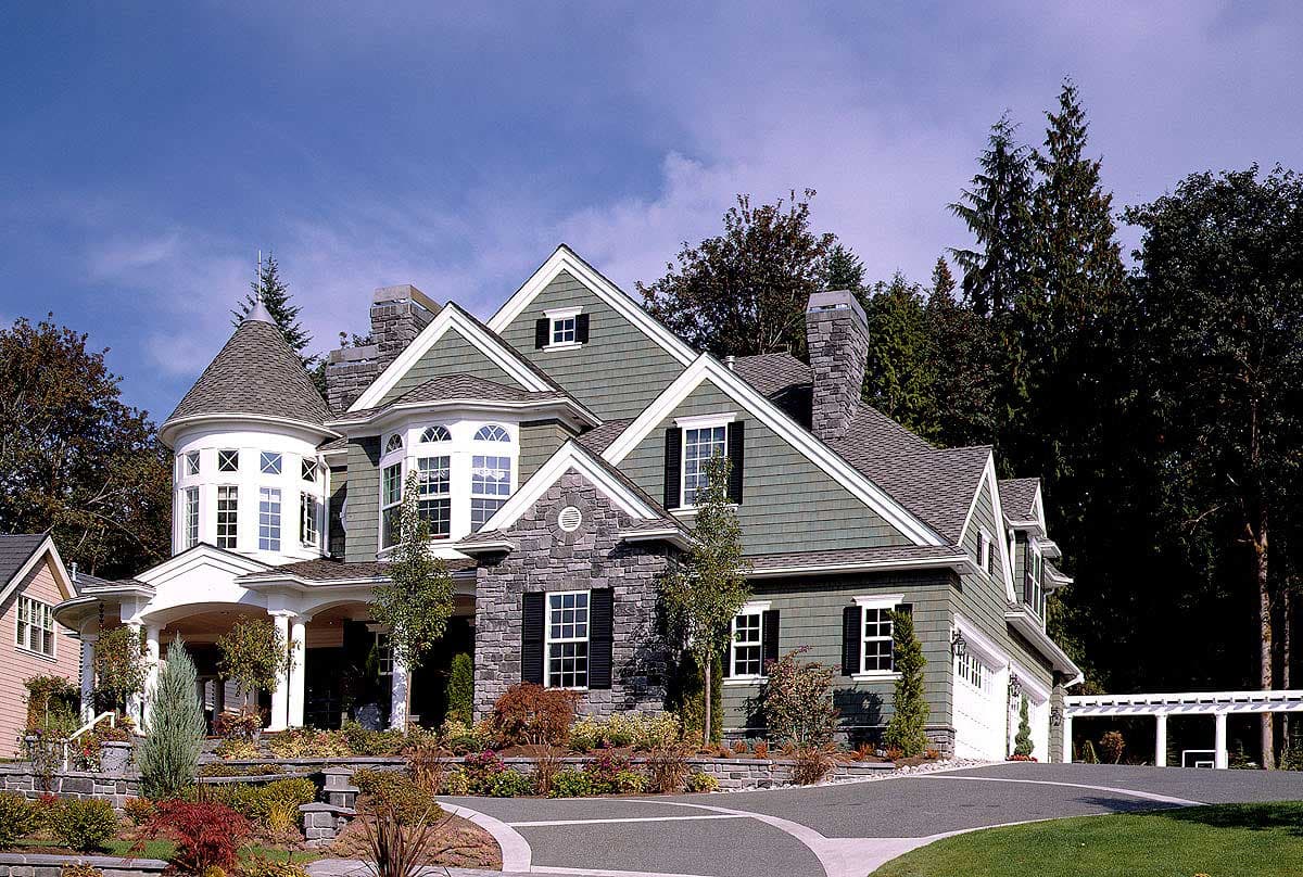 House plan exterior: two-story, green siding, stone accents, prominent gables, turreted corner, and covered porch.