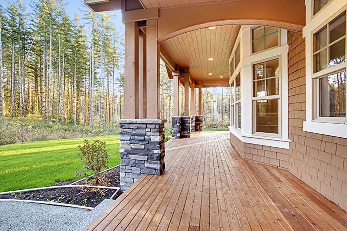 House plan exterior featuring a covered wood deck with stacked stone columns, arched ceiling, and shingle siding.