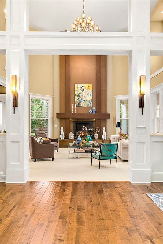 Interior view of a living room featuring a tall fireplace with wood surround, seating area, coffee table, and chandelier.
