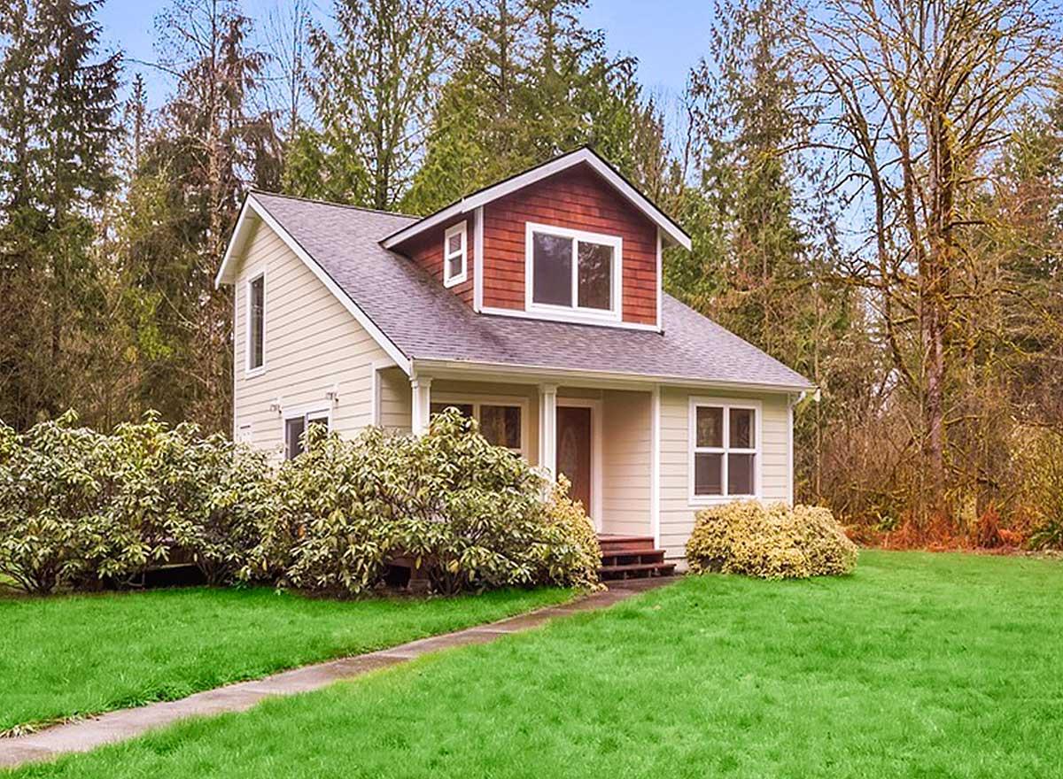 House plan exterior. Two-story cottage style home with a gabled roof, dormer, and small front porch. Light-colored siding and dark roof.