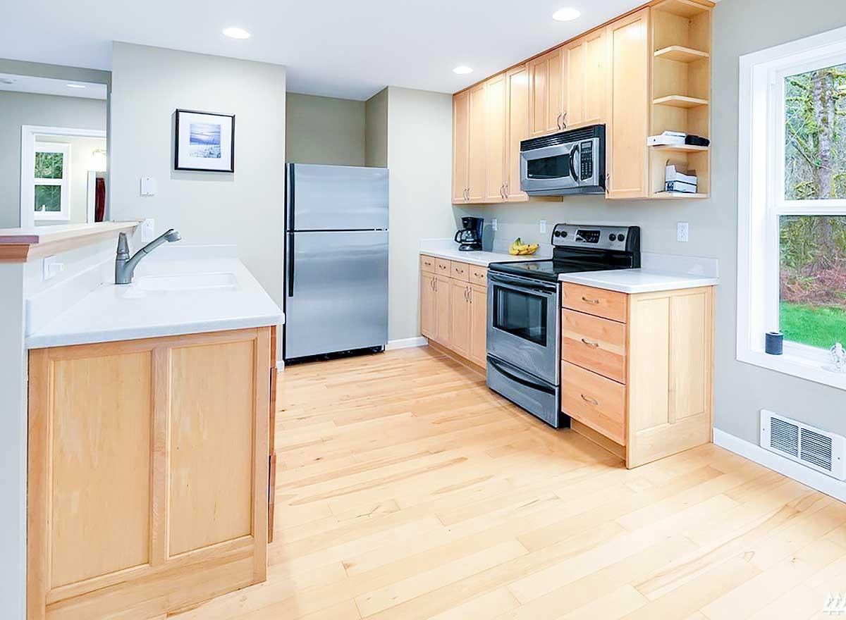 Kitchen with light wood cabinetry, stainless steel refrigerator and range, white countertops, and large window.