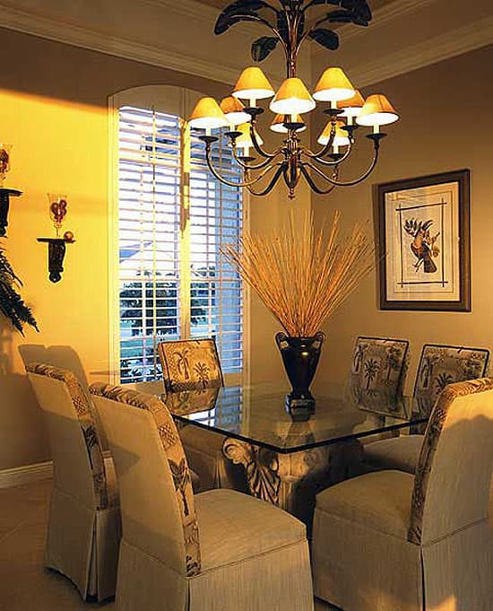 Glass top dining table with ornate base, upholstered chairs, and decorative chandelier.