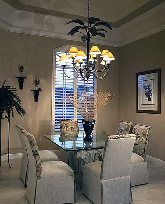 Dining room with glass-top table, upholstered chairs, and a palm tree chandelier.