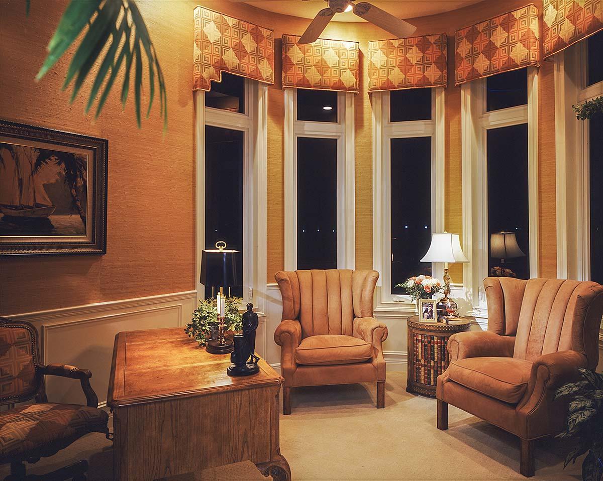 Interior view of a room with a bay window, wingback chairs, a wooden desk, and decorative valances.