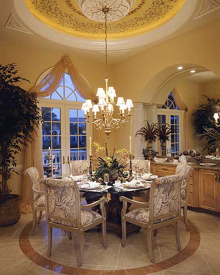 Formal dining room with round table, ornate chandelier, arched windows, and decorative ceiling.
