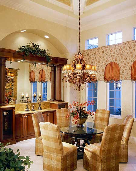 Interior dining room with round table, upholstered chairs, dark wood cabinetry, and ornate chandelier.