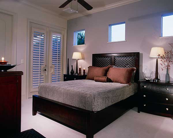 Bedroom with dark wood furniture, large French doors with shutters, and three small square windows.