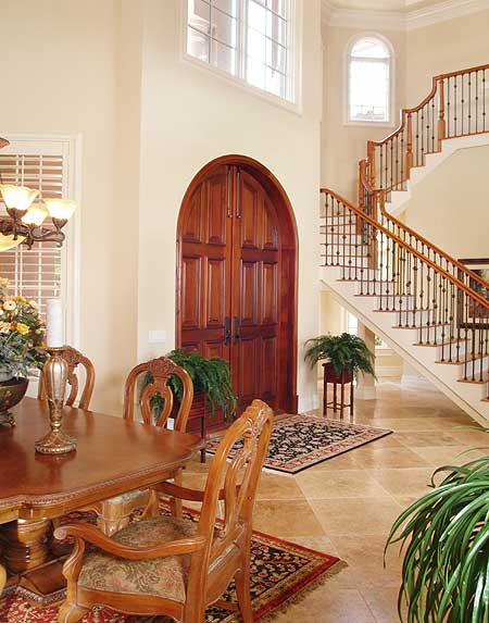 Interior view: Arched double doors and a sweeping staircase with ornate balusters in a grand foyer.