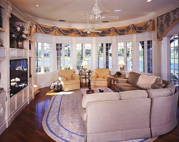 Living room with curved sectional sofa, built-in media unit, and large bay windows overlooking a body of water.