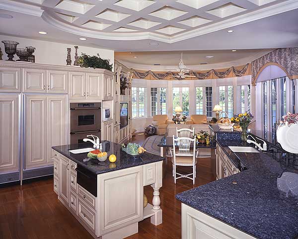 Kitchen with island, integrated oven, and coffered ceiling. Open to a sitting area with bay windows.