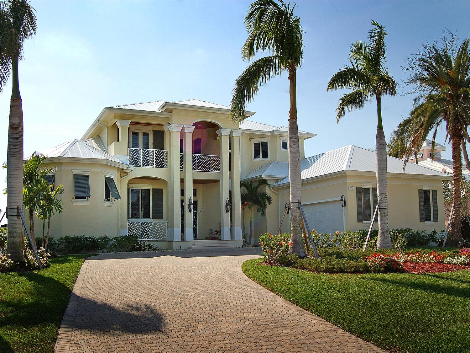Two-story house plan exterior with metal roof, prominent entryway with columns, balconies with decorative railings, and an attached garage.