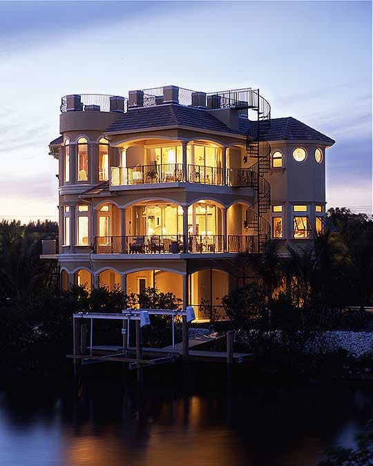 Multi-story house plan exterior with balconies, arched windows, spiral staircase, and rooftop deck by the water.