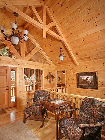 Interior view of a log home great room with vaulted timbered ceiling, fireplace, and wood-paneled walls.