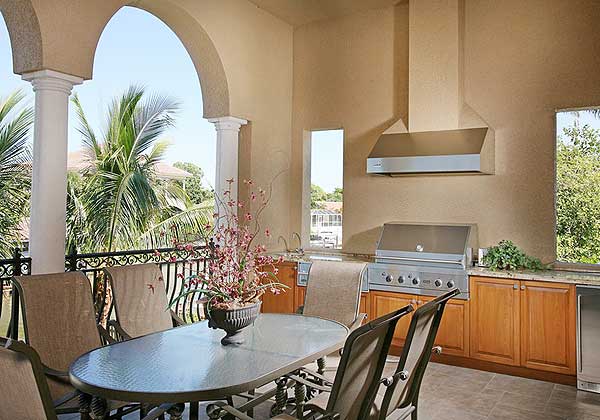 Outdoor kitchen and dining area with a grill, sink, cabinets, and seating under an arched patio.