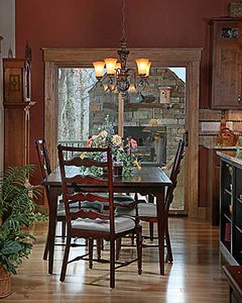 Dining room with dark wood table and chairs, chandelier, and view through large window to stone exterior.