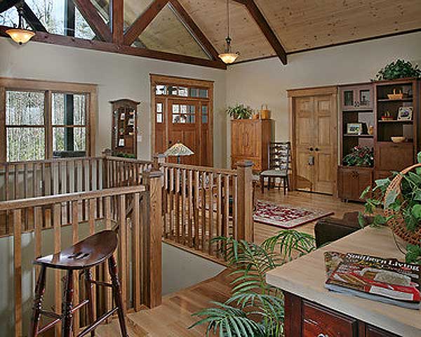Interior view of a great room with vaulted ceiling, exposed beams, wood railings, and a double front door.