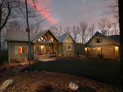 House plan exterior with exposed beams on covered porch, stone accents, and attached two-car garage with gable dormer.