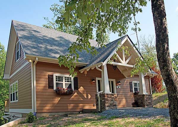 House plan exterior, two stories, timber siding, stone-clad porch columns, and decorative gable brackets.