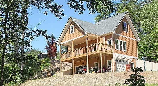 House plan exterior: Two-story home with gabled roof, covered porch, deck, and walk-out basement garage.