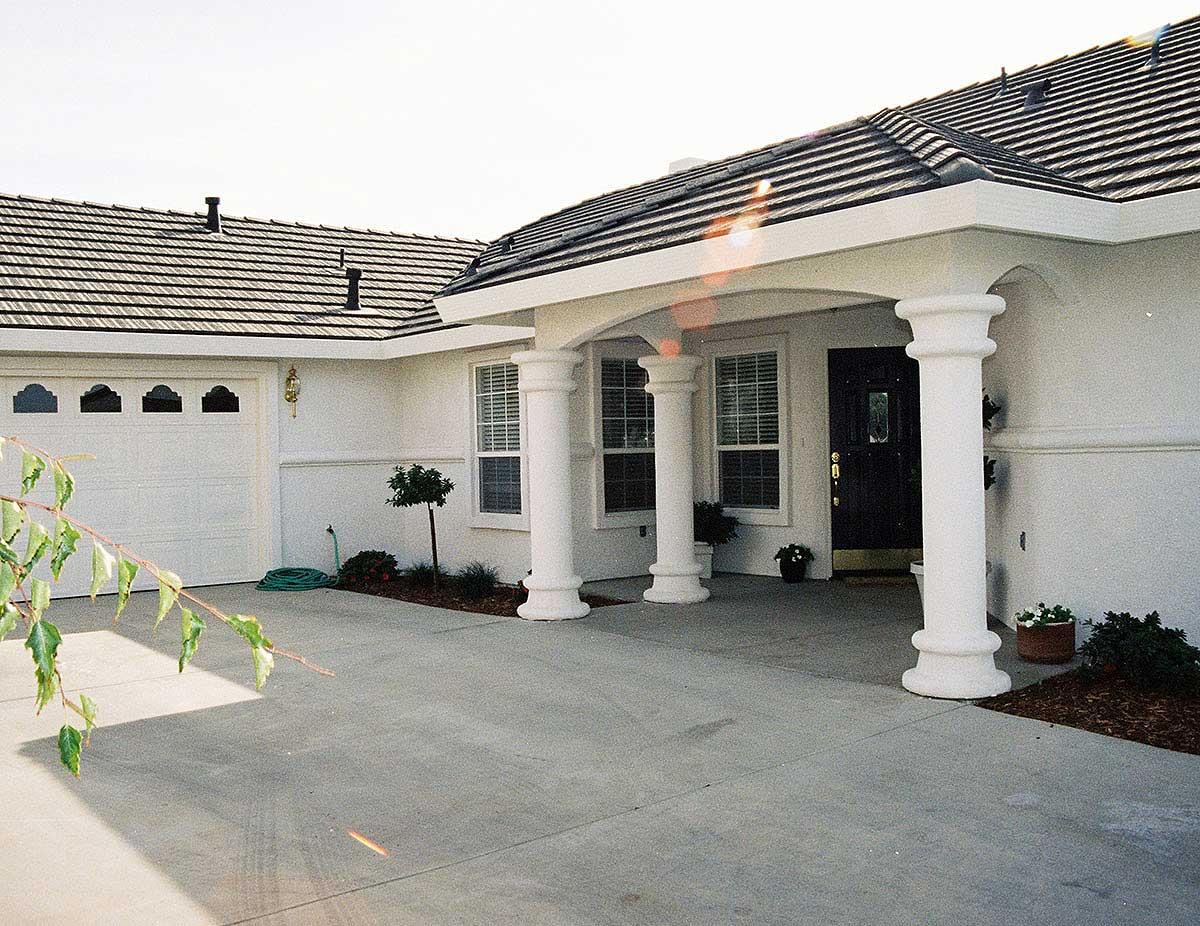 House plan exterior featuring a single-story design with a covered entry supported by Tuscan columns, a two-car garage, and a tile roof.